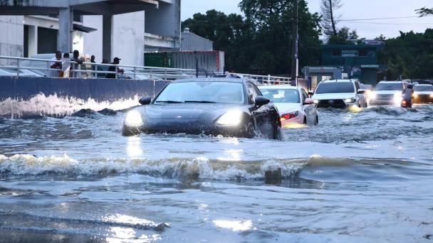 Carros avanzando con el agua sobre las ruedas en una avenida inundada de Santo Domingo