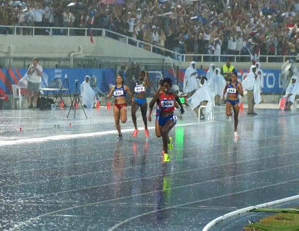 Atletas corriendo los 400 metros bajo un aguacero en el Estadio Olímpico Félix Sánchez, con la pista drenando el agua